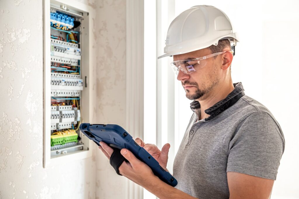 A man wearing a white hard hat uses his tablet to record job updates