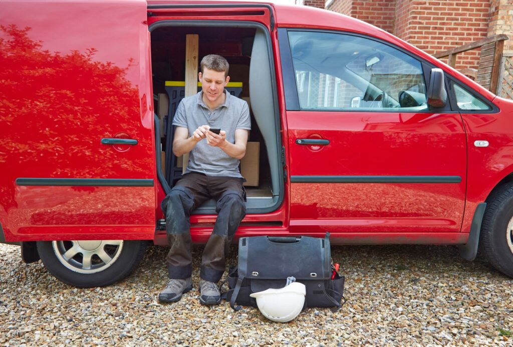 A man sitting in a red van using an app on his phone