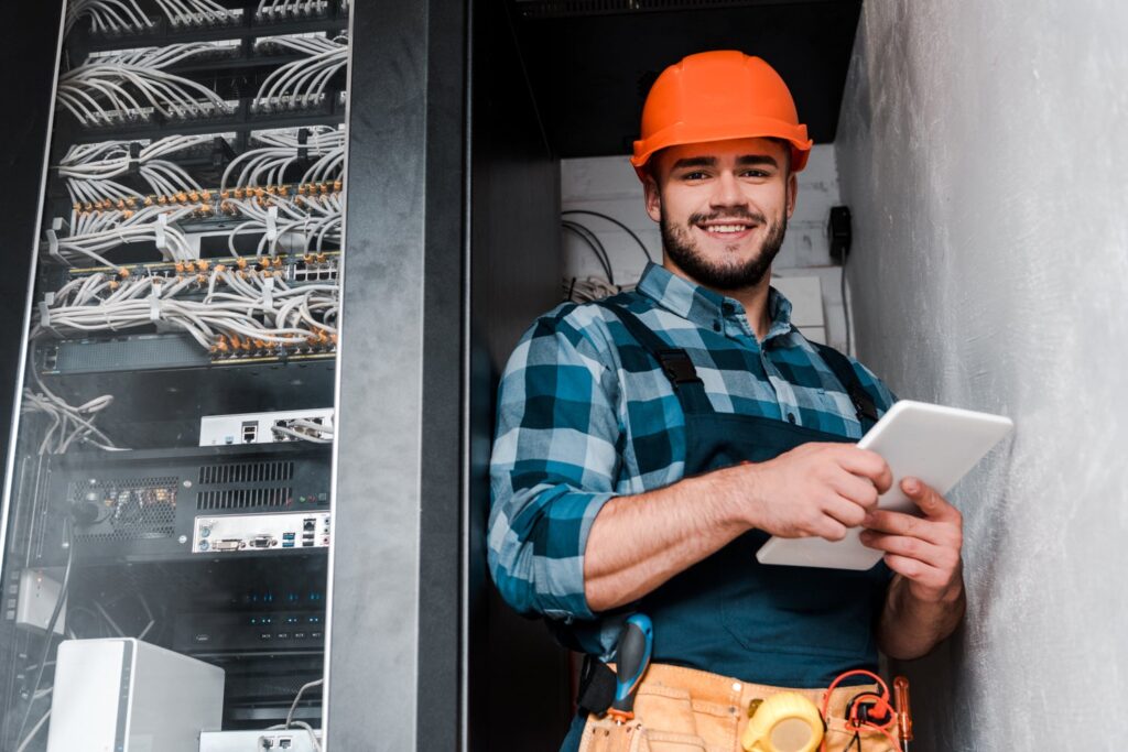 A man in an orange hard hat holding a tablet to upload invoices for making tax digital